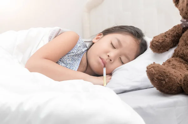 Sjuk flicka ligger i sängen med en termometer — Stockfoto