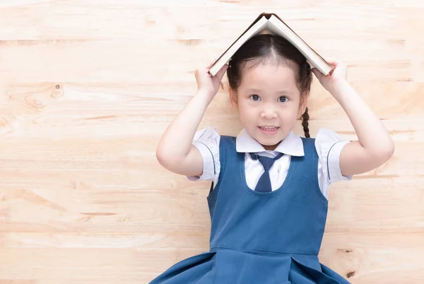 Carino asiatico ragazza sorriso con libro su testa su legno sfondo — Foto Stock