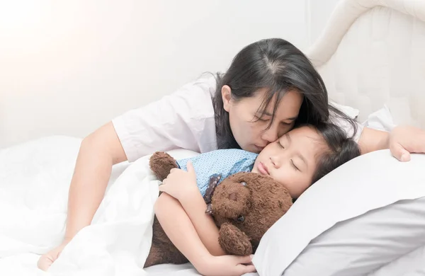 Madre está besando a su hija en la mejilla mientras está acostada en la cama — Foto de Stock