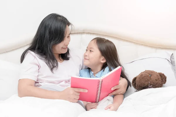 Hija buscando madre leyendo libro en la cama — Foto de Stock