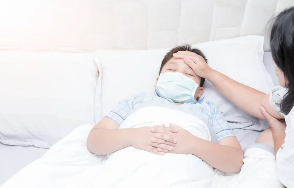 Sjuk pojke med hygienisk mask lägger på säng — Stockfoto