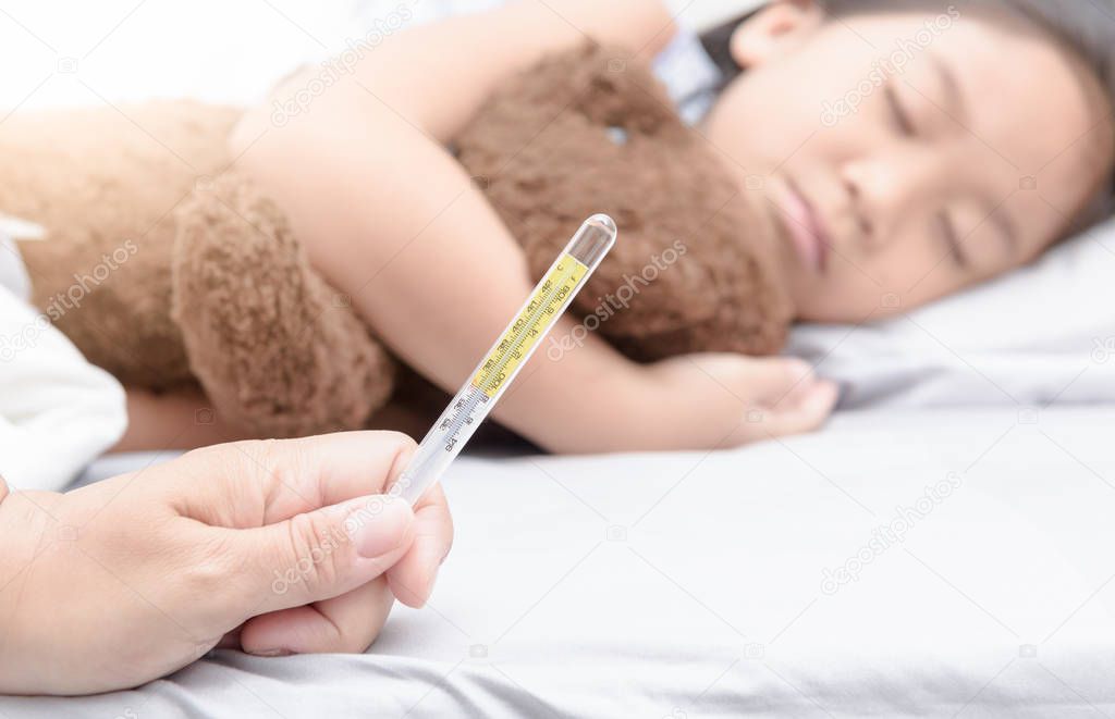 Mother hand holding thermometer and sick girl laying on bed
