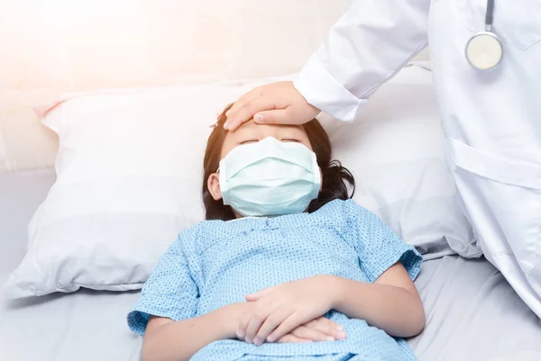 Больная девушка лежит в постели, а доктор рукой измеряет температуру. . — стоковое фото