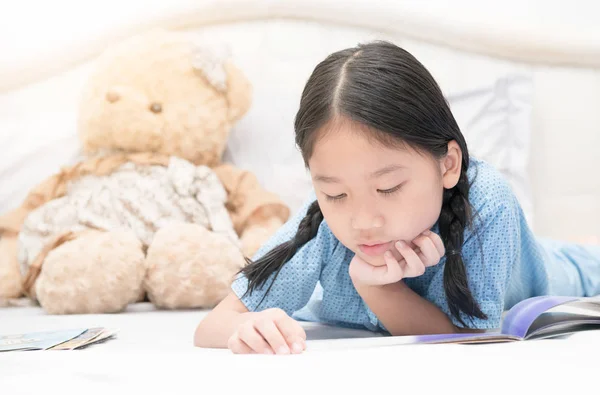 Aranyos ázsiai kislány ágyon mesék olvasása — Stock Fotó