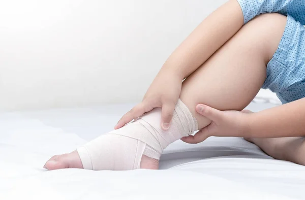 Criança tocando tornozelo com bandagem elástica, perna quebrada — Fotografia de Stock