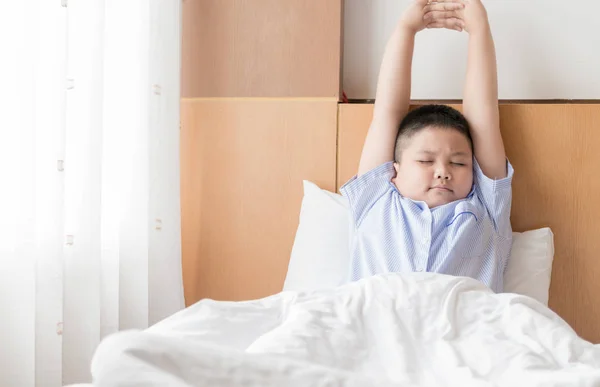 Otyłych tłuszczu chłopiec budzi się i wyciąganie na łóżku. — Zdjęcie stockowe