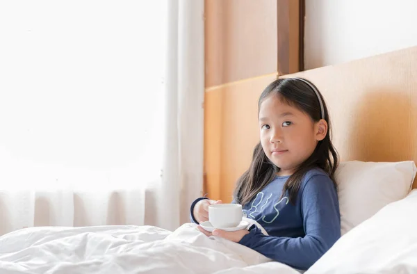 Gadis asia lucu memegang susu panas di tempat tidur — Stok Foto