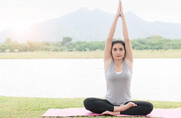 Atractiva joven mujer haciendo ejercicio y sentada en yoga lotus posi — Foto de Stock
