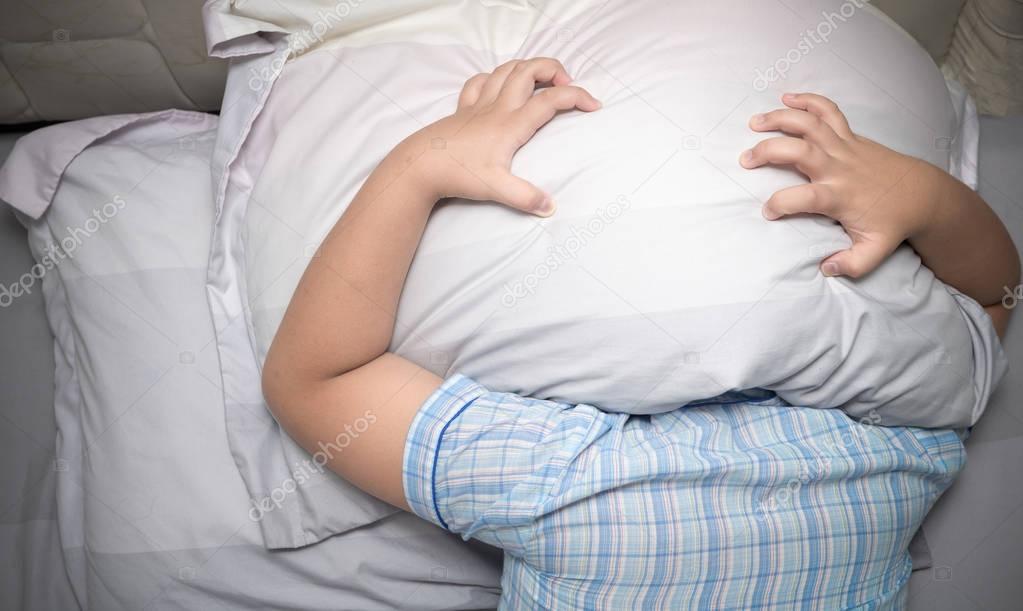 Child lying in bed covering head with pillow