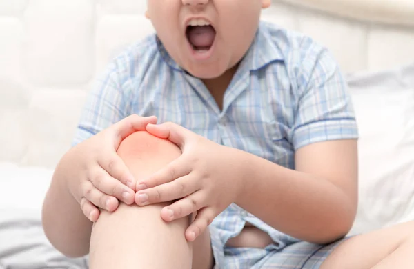 Толстый толстый мальчик страдает от боли в колене и сидеть на кровати — стоковое фото