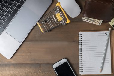 Dizüstü bilgisayar ve boş kağıt ahşap arka plan üzerinde alışveriş sepeti,