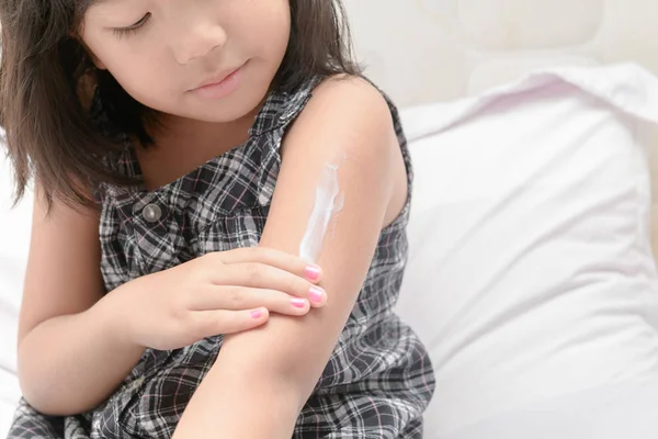 Niña aplicando crema de loción corporal en su brazo . — Foto de Stock