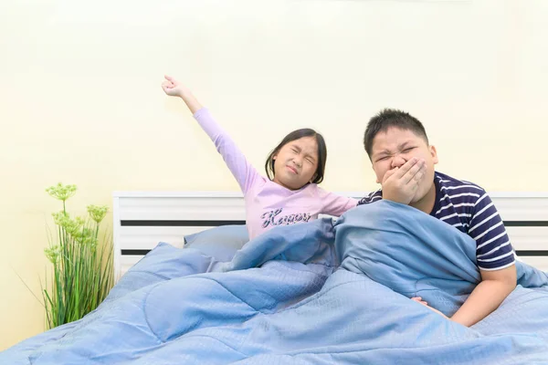 Брат зевает, а сестра растягивается в постели — стоковое фото