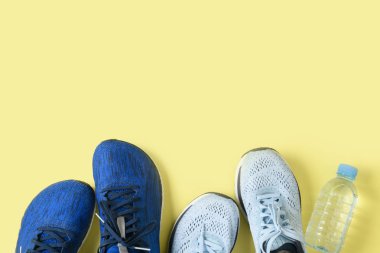 Sarı arka planda iki koşu ayakkabısı ve bir şişe su.,