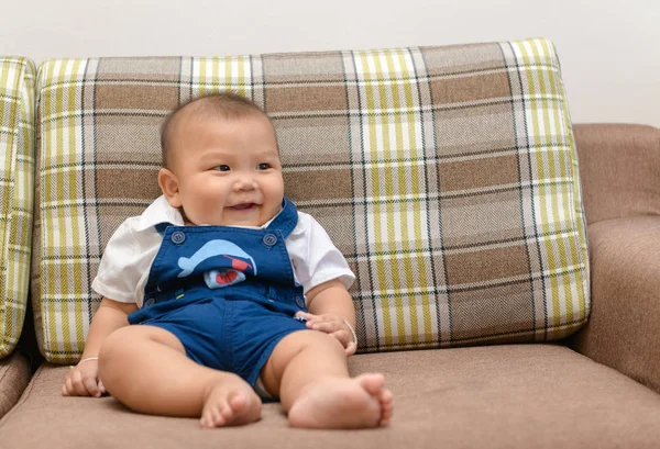 Söt asiatisk bebis sitter och ler på soffan. — Stockfoto
