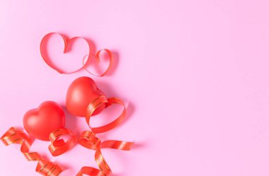 Pembe arka planda kalp hediye kutusu ve kalp kırmızı kurdelesi.