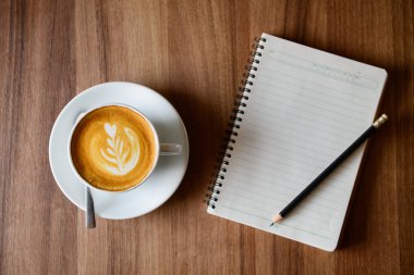 cup of latte art coffee with blank notebook and pencil 