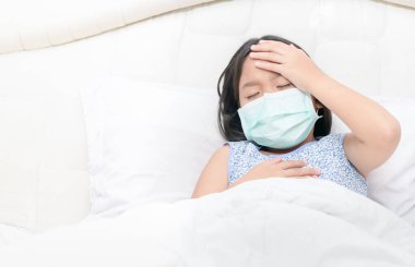 Asyalı bir kız cerrahi maske takıyor yüksek ateş ve baş ağrısı, Wuhan Coronavirüsü ve salgın virüsü olan hasta bir çocuk.