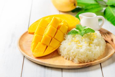 Olgun mango ve hindistan cevizi sütüyle beyaz ahşap arka planda yapışkan pirinç, yaz mevsiminde Tayland tatlısı.