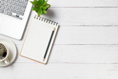 Beyaz ahşap masa boş defter dizüstü bilgisayar ve beyaz ahşap arka planda kahve. Fotokopi alanı, düz yatak ve ev konsepti ile üst görünüm