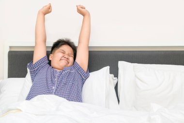Obez şişman çocuk sabah uyanıp yatakta geriniyor, sağlık hizmetleri ve günaydın dünya konsepti.