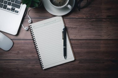 Kalem ve dizüstü bilgisayarlı boş bir defter eski ahşap masa masasında. Koyu tonlu, düz yataklı, kopyalama alanı ile üst görünüm.