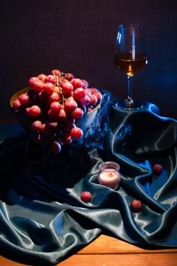 Durgun üzümler ve arka planda mum dumanı olan bir bardak şarap.