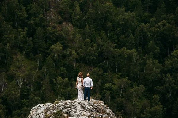 Pareja de bodas en el borde de la montaña. Viaje de bodas. Una pareja amorosa. La pareja tiene las manos en el borde de la roca. Boda en las montañas — Foto de Stock