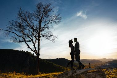 Bir kaç içinde aşk silüeti. Adam ve kız günbatımında sarılma. Çift yayılıyor. Doğa severler. Erkek ve kadın gün batımını izlemek. Gün batımında severler. Dağlarda seyahat. Balayı gezisi