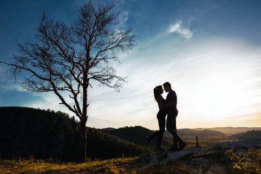 Bir kaç içinde aşk silüeti. Adam ve kız günbatımında sarılma. Çift yayılıyor. Doğa severler. Erkek ve kadın gün batımını izlemek. Gün batımında severler. Dağlarda seyahat. Balayı gezisi