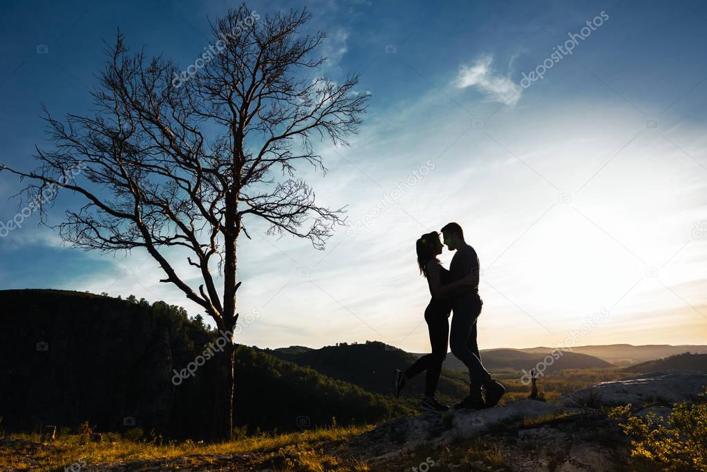 Silhouette of a couple in love. Guy and girl hugging at sunset. Couple travels. Lovers in nature. Man and woman watching the sunset. Lovers at sunset. Travel in the mountains. Honeymoon trip