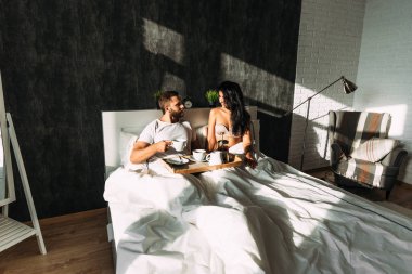Loving couple having breakfast in bed. Guy and girl in bed. Breakfast in bed. Tea in bed. The relationship between a man and a woman. Loving couple. Morning lovers. Family relationships. Good morning