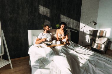 Loving couple having breakfast in bed. Guy and girl in bed. Breakfast in bed. Tea in bed. The relationship between a man and a woman. Loving couple. Morning lovers. Family relationships. Good morning