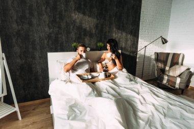 Loving couple having breakfast in bed. Guy and girl in bed. Breakfast in bed. Tea in bed. The relationship between a man and a woman. Loving couple. Morning lovers. Family relationships. Good morning
