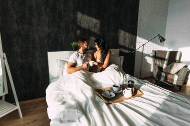 Loving couple having breakfast in bed. Guy and girl in bed. Breakfast in bed. Tea in bed. The relationship between a man and a woman. Loving couple. Morning lovers. Family relationships. Good morning