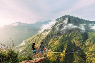 The couple greets the sunrise in the mountains. Boy and girl in the mountains. Man and woman holding hands. The couple travels around Asia. Travel to Sri Lanka. Serpentine in the mountains. Honeymoon clipart