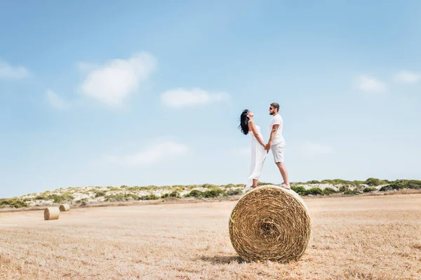Couple in love in the field. A boy and a girl near a haystack.  Round haystack. A man and a woman standing near a haystack. Couple travels. Honeymoon. Newly married couple. Man and woman holding hands