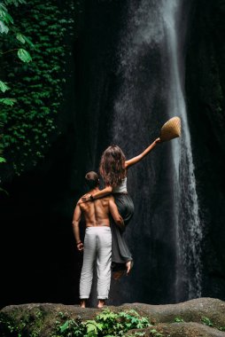 Bir adam şelalede bir kızı kollarında tutuyor. Şelaledeki çift, dikiz manzaralı. Balayı gezisi. Bali 'de tatilde olan mutlu çift. Aşık bir çift dünyayı gezer. Asya 'da tatil, Endonezya.