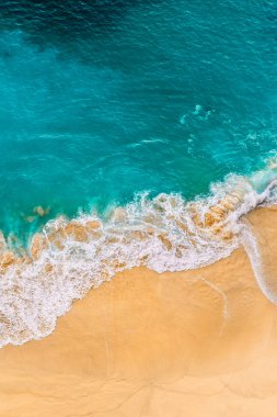Turkuaz denizi ve dikey manzaralı güzel kumlu bir sahil. Tropikal turkuaz okyanus plajı Nusa Penida Bali Endonezya 'nın insansız hava aracı görüntüsü. Güzel dalgaları olan ıssız kumlu bir sahil. Endonezya plajları.