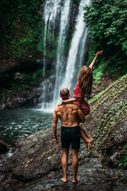Atletik yapılı bir adam şelalede güzel bir kızı kollarında tutuyor. Şelaledeki çift, dikiz manzaralı. Balayı gezisi. Bali 'de tatilde olan mutlu çift. Birbirine aşık bir çift dünyayı gezer..