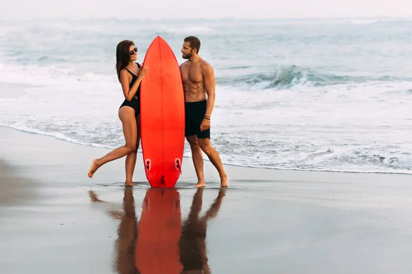 サーフボードとビーチで恋にカップル バリ島の美しいカップル 日没時にビーチのサーフボードの後ろにキスをする幸せなスポーティなカップル 健康的なライフスタイルの概念 — ストック写真