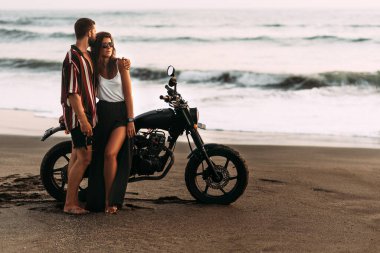 Sahilde motosikletli bir çift. Kumsalda aşık bir çift gün batımıyla tanışır. Bir adam sahilde bir kadını kucaklıyor. Motosikletli güzel bir çift. Motosikletle seyahat et. Kumsalda aşıklar
