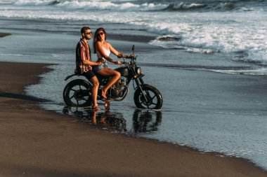 Sahilde motosikletli bir çift. Kumsalda aşık bir çift gün batımıyla tanışır. Bir adam sahilde bir kadını kucaklıyor. Motosikletli güzel bir çift. Motosikletle seyahat et. Kumsalda aşıklar