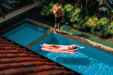 Havuz kenarında dinlenen bir çift. Yurtdışında tatil. Birbirlerine aşık bir çift havuz kenarında güneşleniyor. Bir adam ve bir kadın havuzda yüzüyor. Tatilde bir çift. Erkek ve kız havuzda rahatlar.