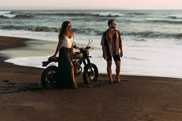 Stylish couple on a motorcycle on the beach. A couple on a motorcycle meets the sunset. Beautiful couple on a motorcycle. Travel on a motorcycle. Lovers at sunset. Journey to the island of Bali