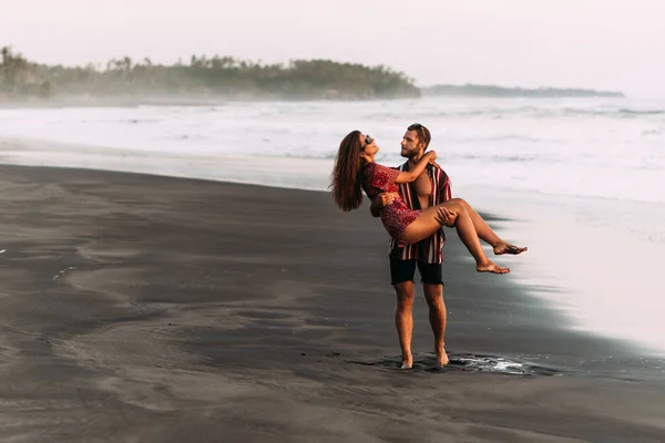 The couple is having fun on the beach. A couple in love at sunset walking along the beach. The man lifted the girl into his arms. Beautiful couple on the beach. Happy couple on vacation in Bali