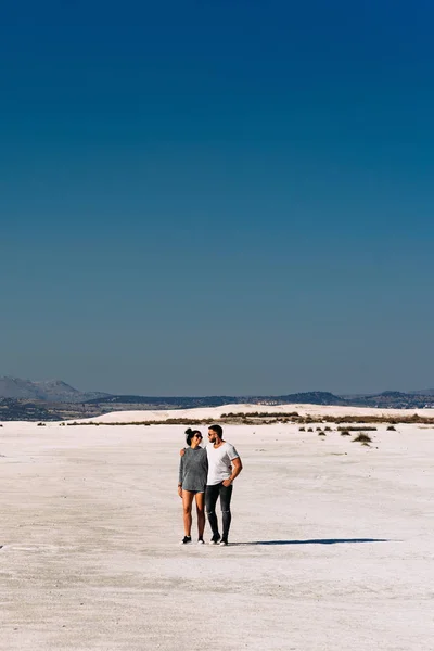 Casal feliz andando na praia de areia vazia. Um casal amoroso caminha ao longo da costa do lago Salda, na Turquia. O casal viaja na Turquia. Um par solitário. Belo casal na natureza. Um homem abraça sua mulher — Fotografia de Stock