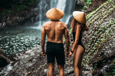 Şelalede aşıklar, dikiz manzarası. Endonezya 'da güzel bir şelaleye hayran olan bir çift. Bali 'de tatilde olan bir çift. Balayı gezisi. Çift Asya 'da seyahat ediyor. Bali adasında tatil.