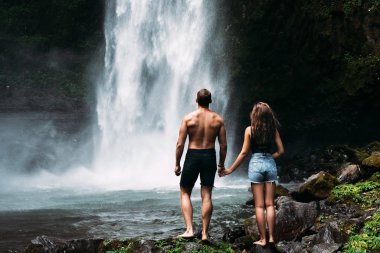 Şelalede aşıklar, dikiz manzarası. Endonezya 'da güzel bir şelaleye hayran olan bir çift. Bali 'de tatilde olan bir çift. Balayı gezisi. Çift Asya 'da seyahat ediyor. Bali adasında tatil.