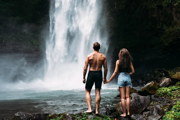 滝で恋人 リアビュー インドネシアの美しい滝を賞賛するカップル バリ島での休暇中のカップル 新婚旅行だ 夫婦はアジアを旅している バリ島での休暇 — ストック写真